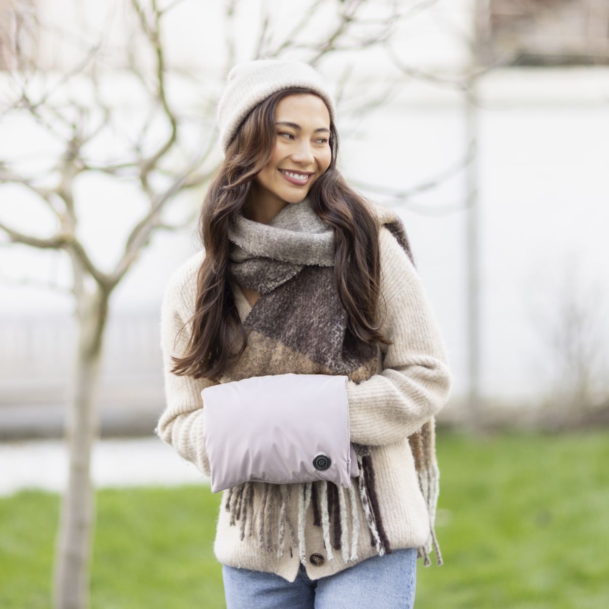 Eine Frau steht im Freien und hält einen kompakten beheizten Handwärmer vor dem Körper.